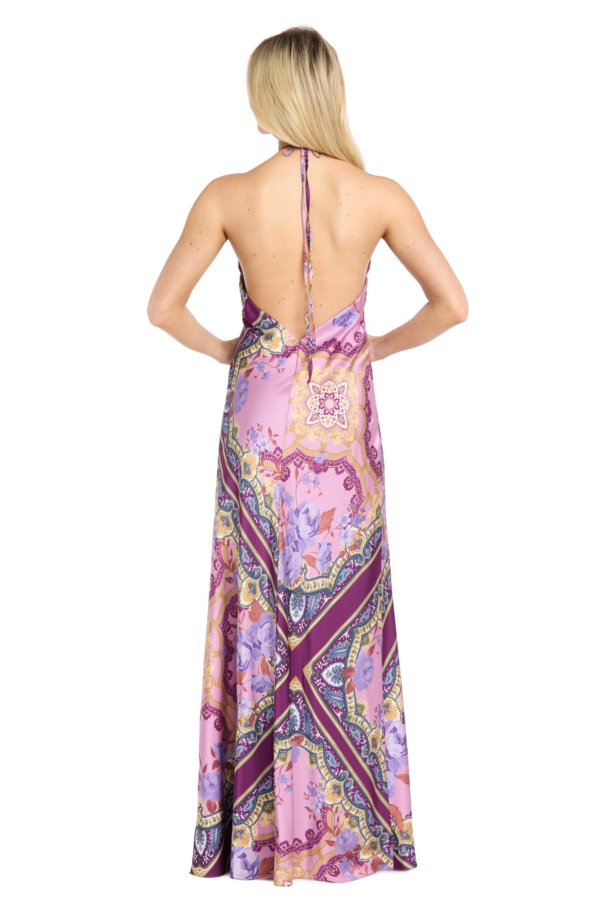 A woman with long blonde hair, facing away from the camera, wears the Paisley Floral Printed Maxi Dress: Morgan 19309โa backless gown featuring a halter neckline and a vibrant purple and pink paisley pattern.